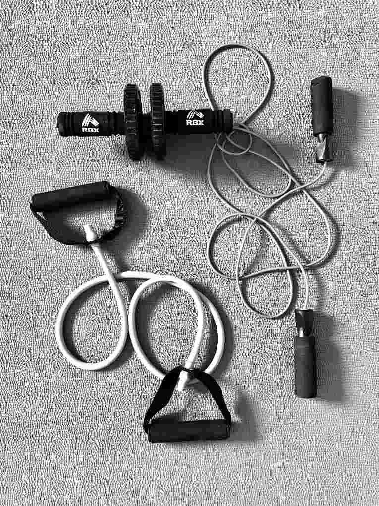 Home workout resistance bands and adjustable dumbbell bar set with jump rope and handles laid out on gym mat for full-body training