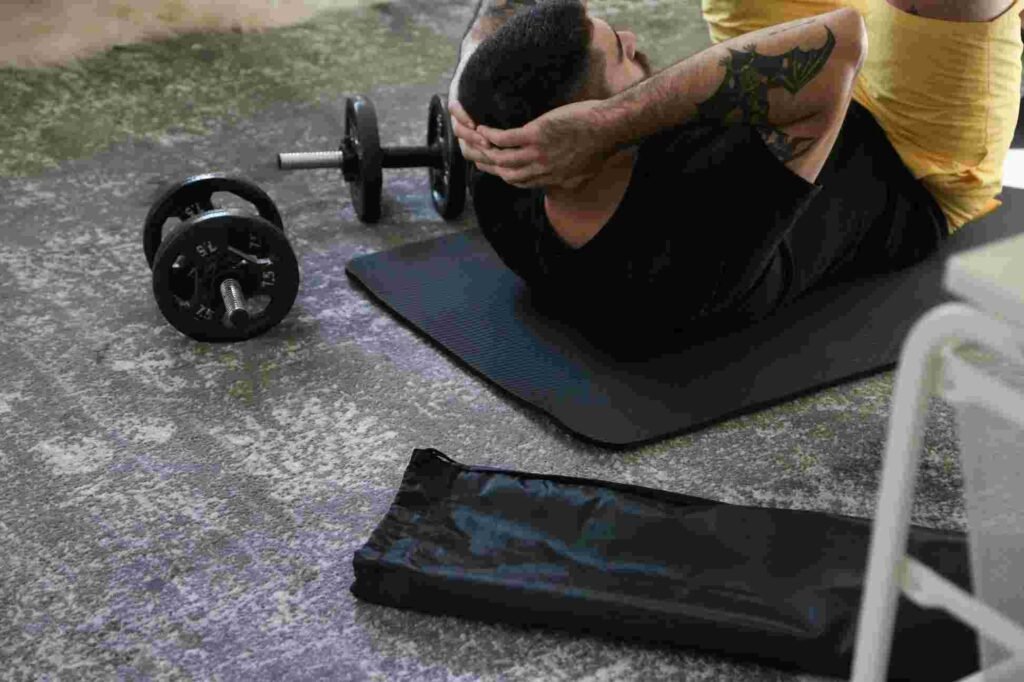 Person performing crunches on a black exercise mat at home gym with dumbbells nearby, focusing on core workout and abdominal strength training