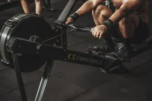 Athlete performing a rowing machine workout in a gym, focusing on full-body cardio and strength training using an indoor rowing machine